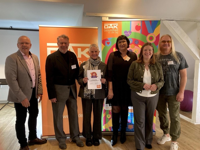 Auf dem Bild sind 6 Menschen bei der Preisverleihung des DAK Wettbewerbs zu sehen. In der Mitte steht Waltraut Klein mit der Urkunde.